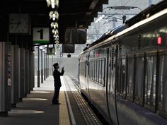 a man standing next to a train at a train station while looking at his cell phone