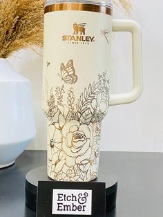 a white coffee cup sitting on top of a black table next to a vase with flowers