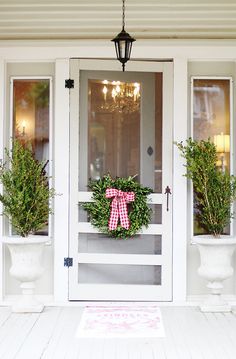 two potted plants on the front porch of a white house with a pink bow