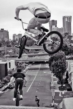 a man on a bike jumping over the street with buildings in the backgroud