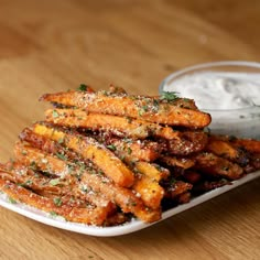 a white plate topped with fried carrots next to a bowl of ranch dressing on a wooden table