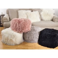 four different colored fur pillows sitting on top of a wooden floor next to a couch