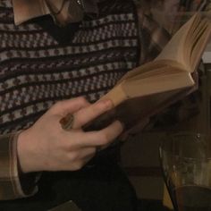 a person sitting down reading a book with their hands on top of an open book