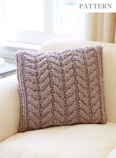 a knitted pillow sitting on top of a white couch in front of a window