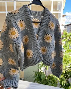 a person holding up a sweater with crocheted sunflowers on the back