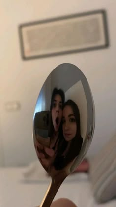 a person holding a spoon with a reflection of two people on it in the mirror