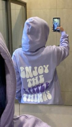 a person taking a selfie in front of a bathroom mirror wearing a purple hoodie