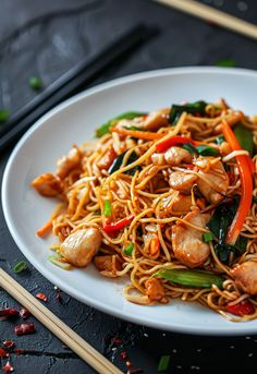 a white plate topped with noodles and vegetables next to chopsticks on a table