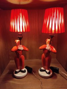 two lamps with red shades on them sitting on a wooden table next to each other