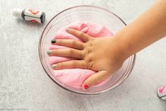 a person's hand on top of a pink substance in a glass bowl next to two rollers