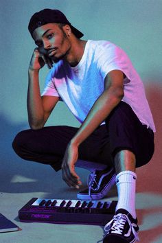 a young man sitting on the ground next to a keyboard and a cell phone in his hand