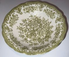 an ornate green and white bowl with flowers on the rim is sitting on a table