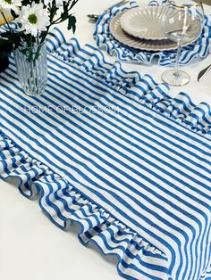 a blue and white striped table cloth with flowers in a vase on the side next to it