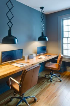 a desk with two computers on it in front of a window and some lights hanging from the ceiling