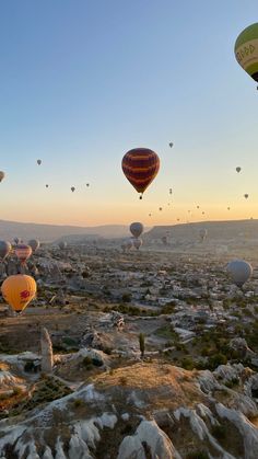 many hot air balloons are flying in the sky over rocks and boulders at sunrise or sunset