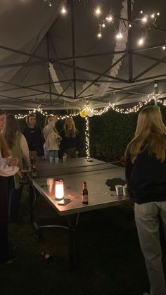 a group of people standing around a ping pong table with lights on the ceiling