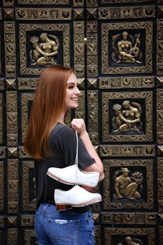 a woman with long red hair is holding two pairs of shoes in front of a wall