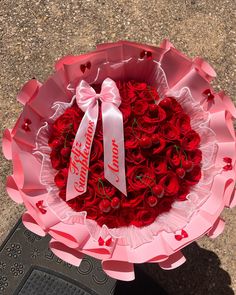 a bouquet of red roses in a pink paper wrapper with a white ribbon tied around it