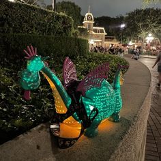 a colorfully lit dragon statue sitting on the side of a road next to bushes