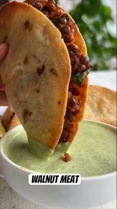 a tortilla being dipped into a bowl filled with guacamole sauce