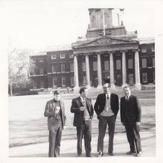 four men standing in front of a building with columns and pillars on the top floor