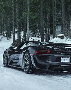 a black sports car parked on the side of a snow covered road in front of trees