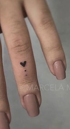 a small black heart tattoo on the middle finger is shown in front of a woman's hand