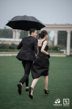 a man and woman walking in the grass with an umbrella