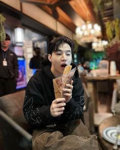 a young man sitting down while eating some kind of food with his mouth wide open