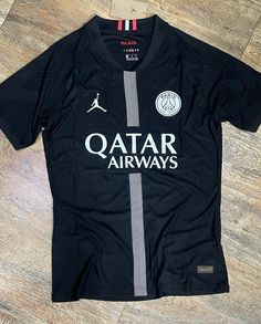 a black shirt with the word qatar airways printed on it, sitting on a wooden floor