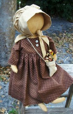 a teddy bear wearing a brown dress and hat sitting on a wooden bench in the park