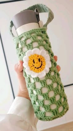 a woman holding a green crocheted water bottle with a smiley face on it