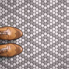 a pair of brown shoes sitting on top of a white and gray tile covered floor