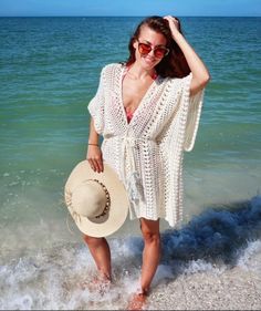 a woman standing on the beach wearing a white crochet cover up and hat