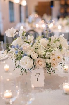 white flowers and greenery are arranged in the centerpieces on this elegant table