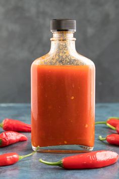 a bottle filled with red peppers sitting on top of a blue tablecloth next to some cut up carrots