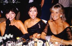 three women sitting next to each other at a table with drinks in front of them