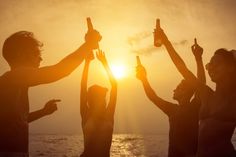 group of people raising their hands in the air at sunset on the beach with sun setting behind them