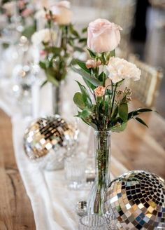 there are many vases with flowers and disco balls on the long table runneres