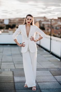 a woman standing on top of a roof with her hands on her hips and wearing a white suit