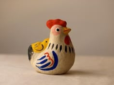 a small ceramic chicken sitting on top of a white tablecloth covered floor next to a gray wall