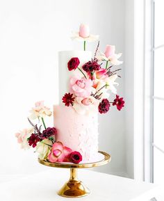 a three tiered cake with pink and red flowers on top is sitting on a gold plate