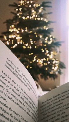 an open book sitting in front of a christmas tree