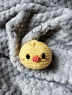 a crocheted yellow chick keychain laying on a gray blanket