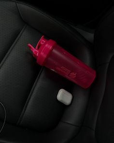 a red bottle sitting on top of a car seat next to an earbud