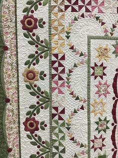 a quilted wall hanging with flowers and leaves on the front, along with an ornate border