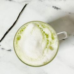 there is a drink with green liquid in the glass on the marble counter top next to an empty straw