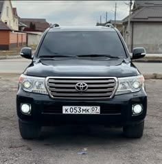 the front end of a black suv parked in a parking lot next to some houses