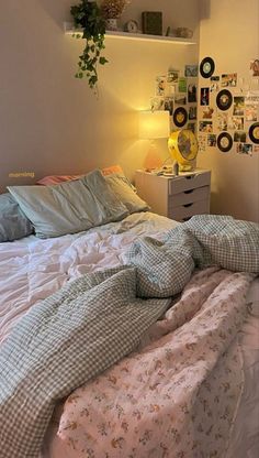 an unmade bed in a bedroom with many pictures on the wall above it and a lamp next to it