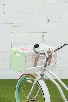 a white bicycle with a green basket on the front wheel and handlebars parked in grass